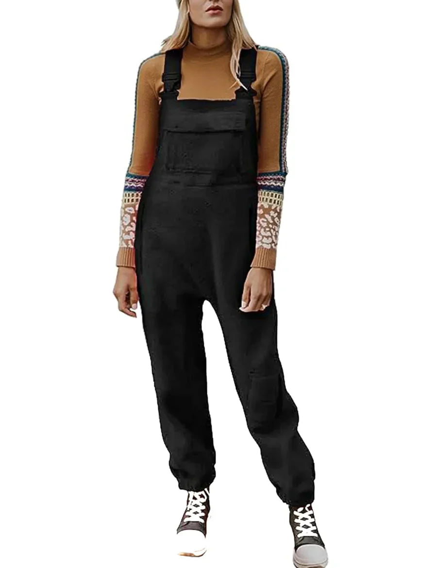 Femme portant une salopette noire, pull marron à motifs, baskets blanches. Mode décontractée, tendance automne, tenue confortable.