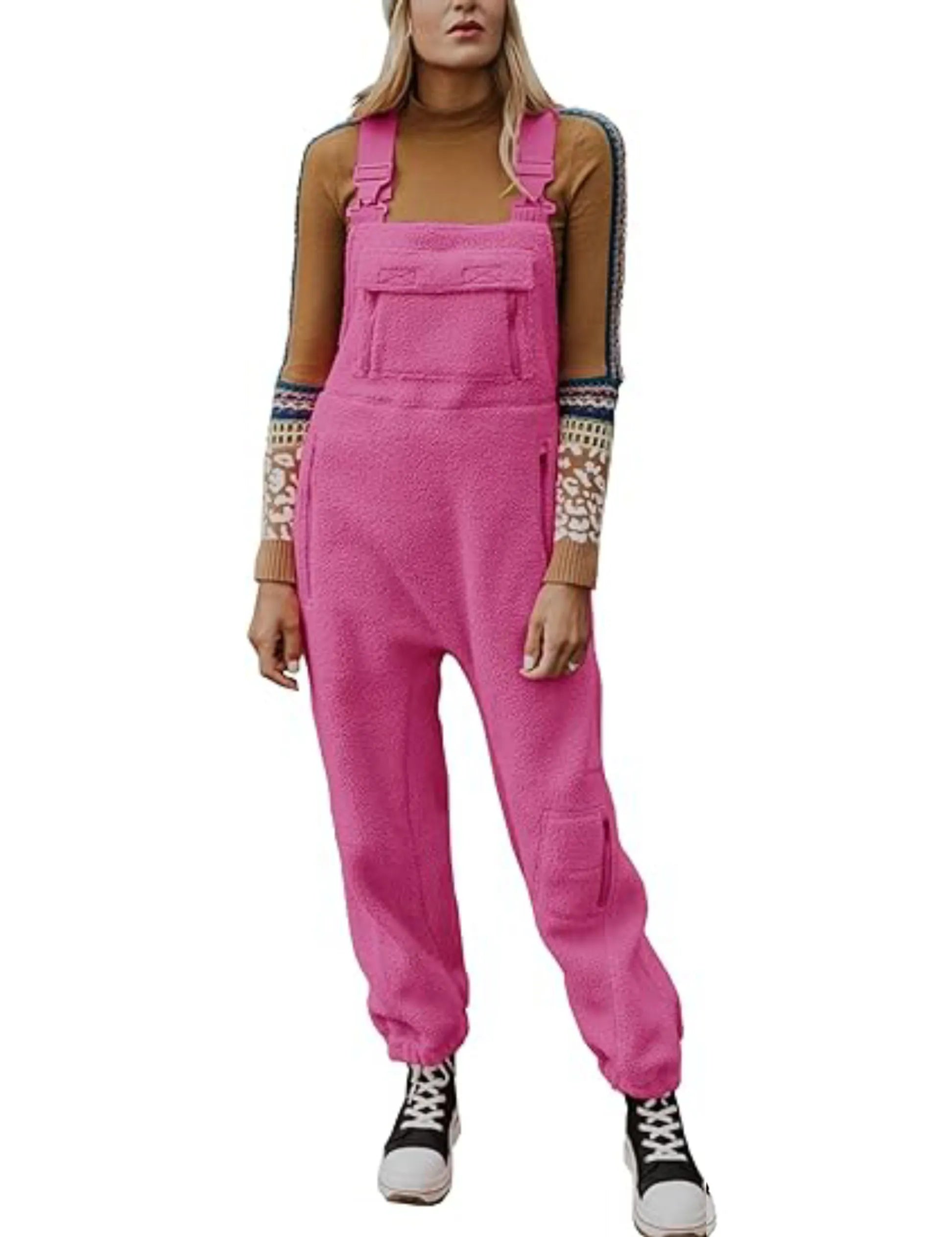 Femme portant une salopette rose en laine polaire, pull marron à motifs, baskets noires et blanches. Mode décontractée, tendance automne-hiver.