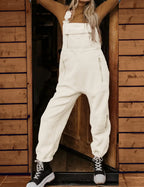 Salopette en laine blanche, style décontracté, portée avec des bottes noires, devant une porte en bois. Mode automne-hiver, tendance et confortable.