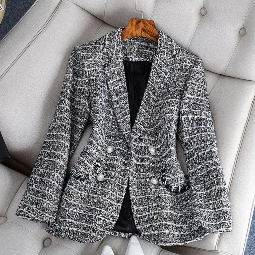 Veste en tweed gris pour femme, élégante et chic, posée sur un fauteuil beige. Mode automne-hiver, style classique, boutons décoratifs.