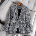 Veste en tweed gris pour femme, élégante et chic, posée sur un fauteuil beige. Mode automne-hiver, style classique, boutons décoratifs.