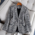Veste en tweed gris pour femme, élégante et chic, posée sur un fauteuil beige. Mode automne-hiver, style classique, boutons décoratifs.