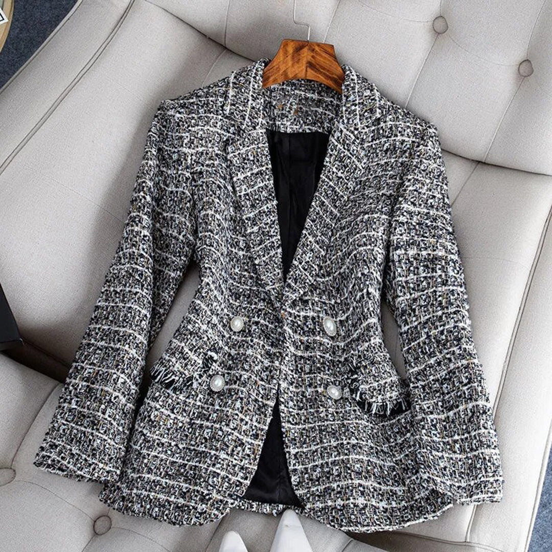 Veste en tweed gris pour femme, élégante et chic, posée sur un fauteuil beige. Mode automne-hiver, style classique, boutons décoratifs.