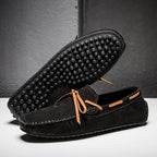 Mocassins en daim noir avec semelle à picots en caoutchouc, lacets marron, posés sur fond gris. Chaussures élégantes et confortables pour hommes.