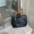 Sac à main en cuir noir avec anses marron posé sur un sol en pierre devant une vitrine de café. Accessoire mode élégant et tendance.