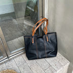 Sac à main en cuir noir avec anses marron posé sur un sol en pierre devant une vitrine de café. Accessoire mode élégant et tendance.