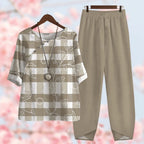 Tenue décontractée femme : chemisier à carreaux beige et blanc avec motifs floraux, collier pendentif, pantalon ample beige, fond fleuri.