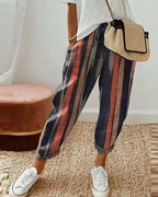 Pantalon rayé multicolore femme, style décontracté, avec sac en paille et baskets blanches. Mode tendance, tenue estivale chic et confortable.