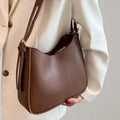 Sac à main marron élégant porté par une personne en veste blanche, design moderne, cuir lisse, idéal pour mode féminine et accessoires tendance.