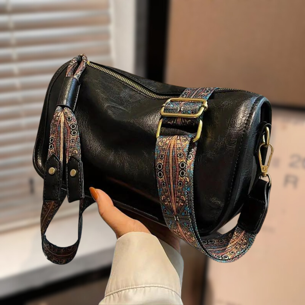 Sac à main en cuir noir avec bandoulière ornée de motifs colorés, tenu par une main. Accessoire de mode élégant et tendance pour femmes.