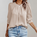 Blouse beige élégante avec manches longues, col plissé, portée avec un jean bleu clair. Mode féminine chic et décontractée.