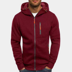 Homme portant un sweat à capuche bordeaux avec fermeture éclair, poches zippées et cordons. Mode décontractée, vêtement automne-hiver tendance.