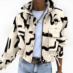 Veste camouflage beige et noire, style militaire, avec poches et cordons, portée par une personne en jean et t-shirt blanc, chaîne dorée visible.