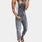 Salopette en jean gris délavé pour femme, avec déchirures stylisées, portée avec un débardeur blanc. Mode décontractée, tendance urbaine.