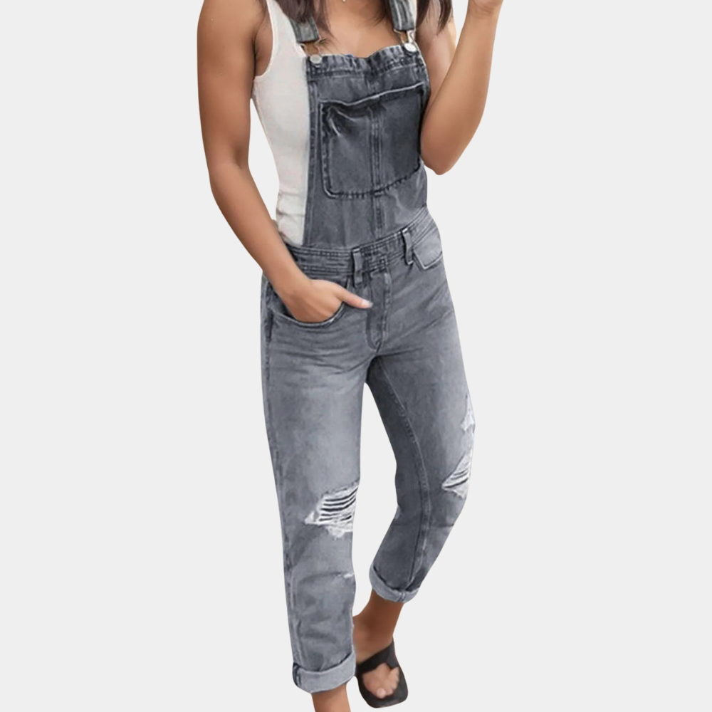 Salopette en jean gris délavé pour femme, avec déchirures stylisées, portée avec un débardeur blanc. Mode décontractée, tendance urbaine.