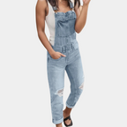 Femme portant une salopette en jean bleu clair avec déchirures, associée à un débardeur blanc et des sandales noires. Mode décontractée tendance.