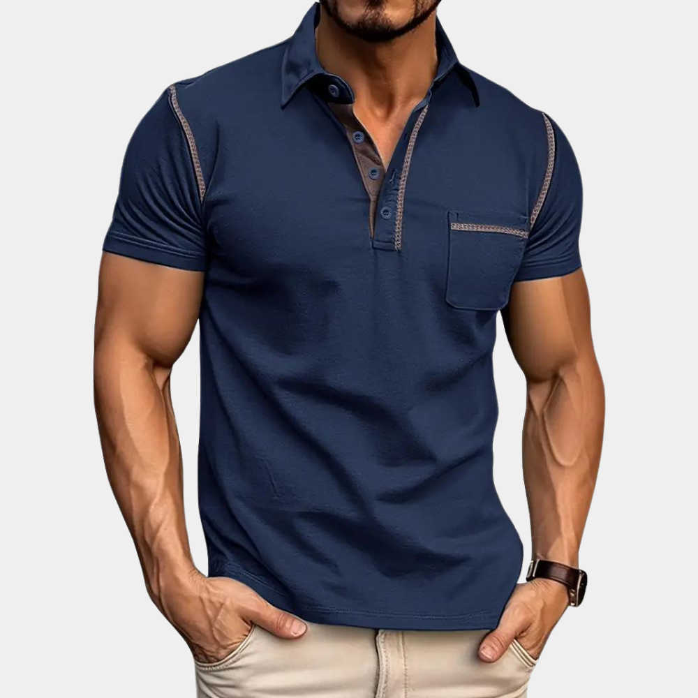 Homme portant un polo bleu marine ajusté avec coutures contrastées, manches courtes, poche poitrine, et pantalon beige. Mode masculine élégante.