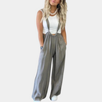 Femme portant une salopette ample grise avec un débardeur blanc et des baskets blanches. Mode décontractée, tendance, style urbain.