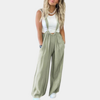 Femme portant une salopette verte ample avec un débardeur blanc, collier tendance et baskets blanches. Mode décontractée chic pour femme.