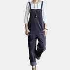 Salopette en velours côtelé bleu marine pour femme, avec poches avant, portée sur un t-shirt blanc à manches longues. Mode décontractée élégante.