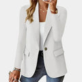 Femme portant un blazer blanc élégant, chemise blanche, jeans, et bijoux dorés. Mode féminine chic, tenue décontractée, style moderne.