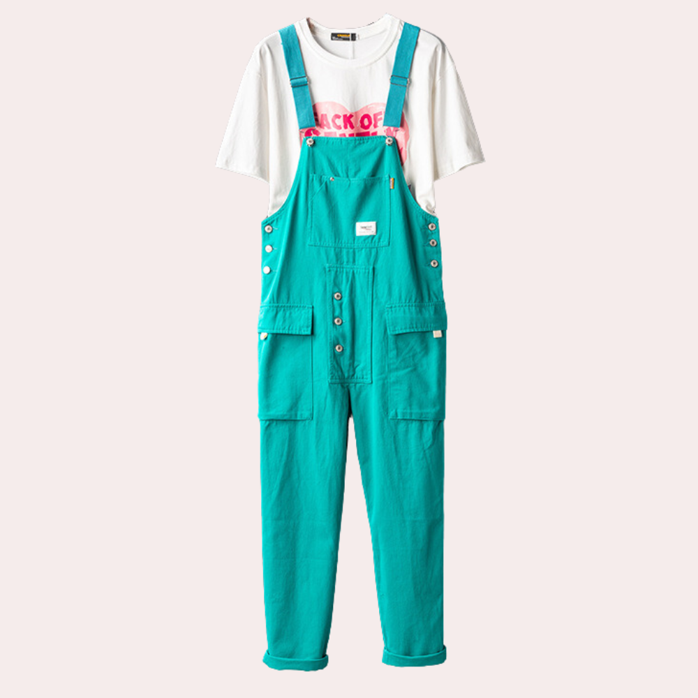 Salopette turquoise en coton avec boutons argentés, poches avant, portée sur un t-shirt blanc imprimé rose. Mode décontractée, tendance urbaine.
