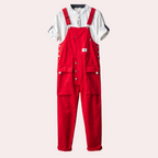 Salopette rouge en coton avec boutons argentés, portée sur une chemise blanche à manches courtes. Mode décontractée, tendance et moderne.
