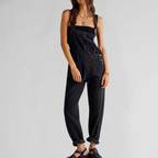 Femme portant une salopette noire en denim, style décontracté, avec des sandales noires. Mode tendance, tenue casual chic, look urbain moderne.