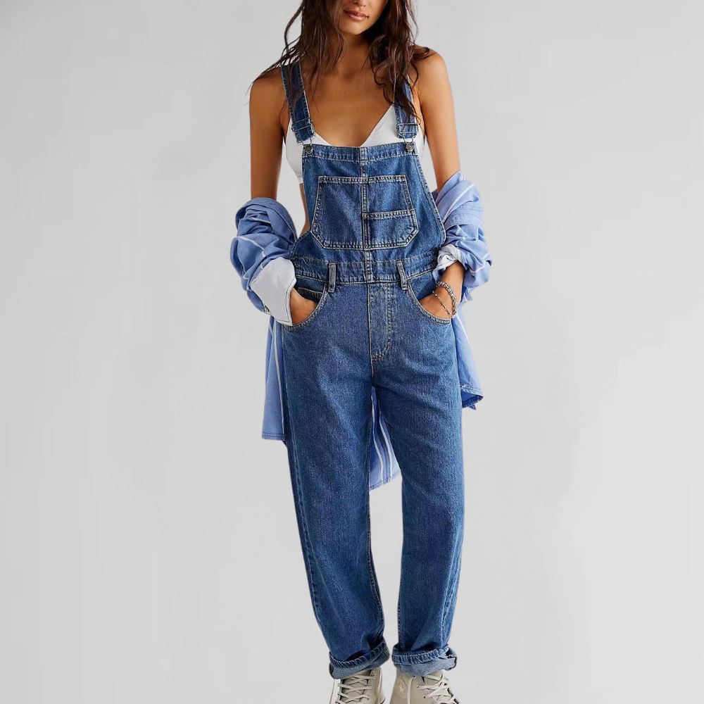 Femme portant une salopette en jean bleu, chemise bleue et baskets blanches. Mode décontractée, tendance denim, style urbain.