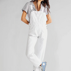 Femme portant une salopette blanche et un t-shirt rayé, posant avec des baskets bleues. Mode décontractée, style urbain, tendance féminine.