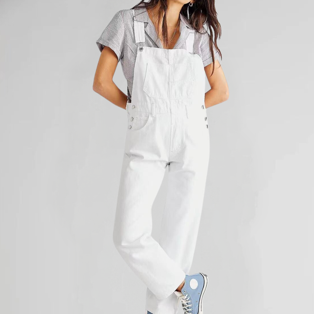 Femme portant une salopette blanche et un t-shirt rayé, posant avec des baskets bleues. Mode décontractée, style urbain, tendance féminine.