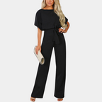 Combinaison noire élégante pour femme avec ceinture, manches courtes, tenue chic, accessoirisée d'une pochette beige, mode tendance.