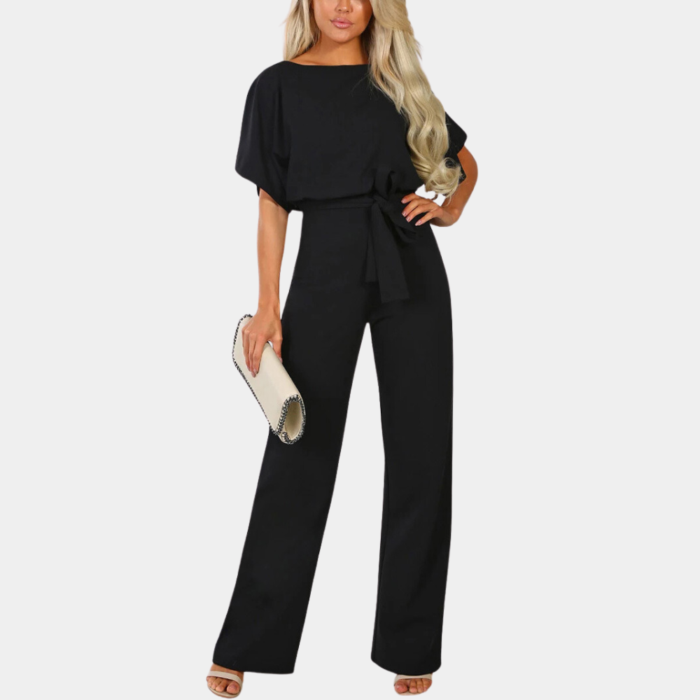 Combinaison noire élégante pour femme avec ceinture, manches courtes, tenue chic, accessoirisée d'une pochette beige, mode tendance.