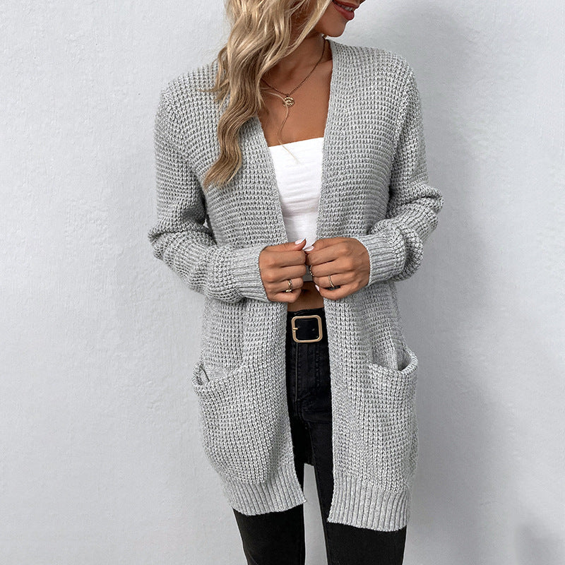 Femme portant un cardigan gris en tricot, débardeur blanc et jean noir. Mode automne, style décontracté, tenue élégante et confortable.