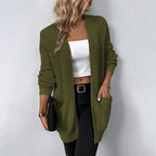 Femme portant un cardigan vert olive, top blanc, pantalon noir, tenant une pochette noire. Mode automne, style décontracté, tendance féminine.