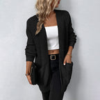 Femme portant un cardigan noir en maille, top blanc court, pantalon noir, accessoirisée d'une pochette et bracelet doré. Mode automne chic.