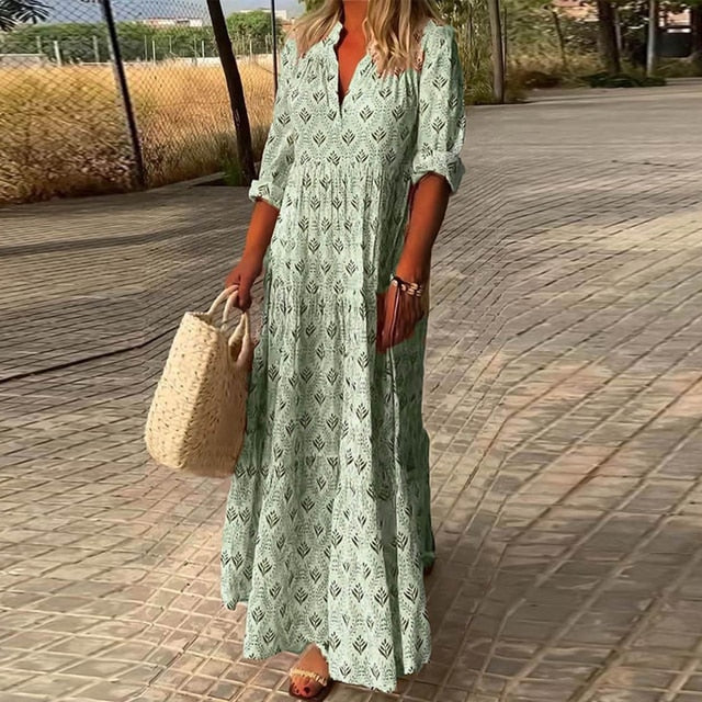 Femme en robe longue verte à motifs, portant un sac en osier, marchant sur un chemin pavé. Mode estivale, tenue décontractée, style bohème.