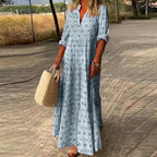 Robe longue bohème bleue à motifs géométriques, femme tenant un sac en osier, promenade sur chemin pavé, style estival décontracté.