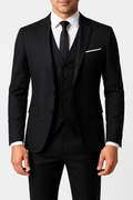 Homme en costume noir élégant avec cravate, chemise blanche et pochette, posant sur fond blanc. Mode masculine, tenue formelle, style classique.