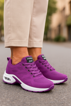 Chaussures de sport violettes pour femme sur trottoir, design moderne avec semelle blanche, idéales pour la marche et le fitness urbain.