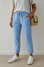 Personne portant un pantalon bleu clair avec cordon, t-shirt blanc, baskets blanches et sac en osier. Mode décontractée, style estival.