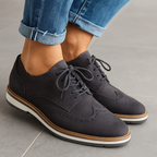 Chaussures derby en cuir noir pour femme, avec semelle blanche et détails perforés, portées avec un jean retroussé. Mode élégante et moderne.