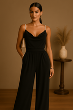 Femme élégante en combinaison noire, posant dans un intérieur minimaliste avec vase décoratif. Mode chic, style moderne, tenue soirée.
