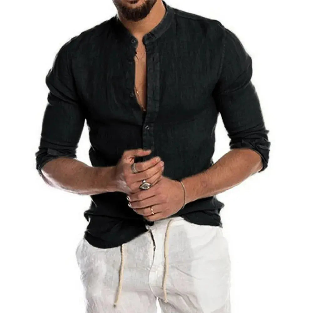 Homme portant une chemise noire à col mao et manches longues, associée à un pantalon blanc. Mode masculine élégante et décontractée.