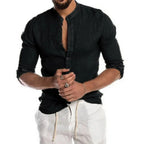 Homme portant une chemise noire à col mao et manches longues, associée à un pantalon blanc. Mode masculine élégante et décontractée.