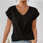 Femme portant un t-shirt noir à col en V, manches courtes, avec colliers dorés, posant contre un mur blanc texturé. Mode décontractée élégante.