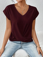 Femme portant un t-shirt bordeaux à col en V, manches courtes, assise sur un canapé, avec un collier doré et un jean décontracté. Mode féminine élégante.
