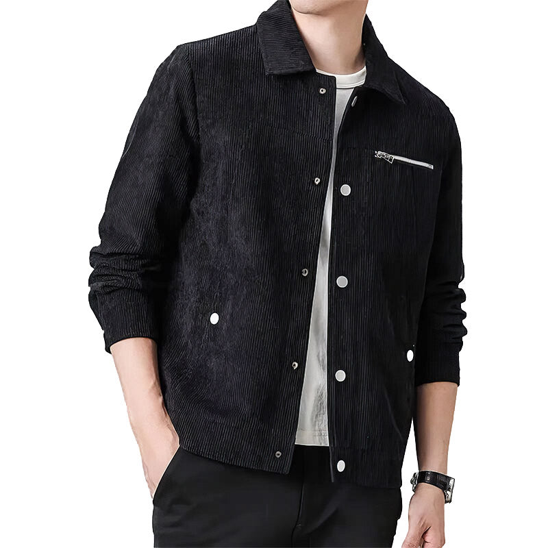 Homme portant une veste noire en velours côtelé avec boutons blancs, poche zippée, chemise blanche et pantalon noir. Mode masculine élégante.