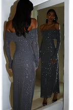 Femme en robe longue pailletée grise, épaules dénudées, se regardant dans un miroir. Mode élégante, tenue de soirée glamour.