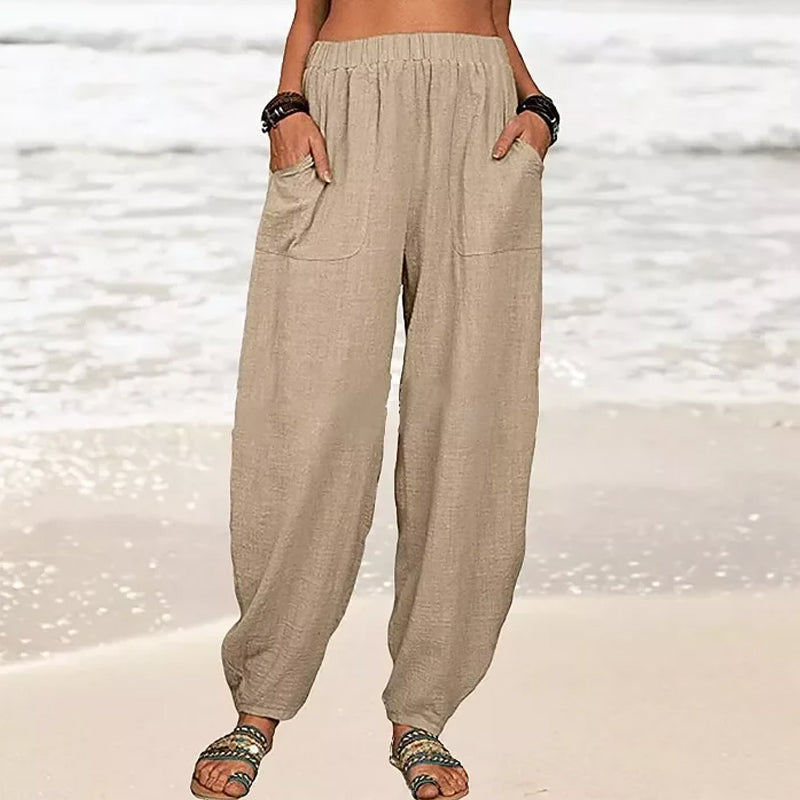 Pantalon ample en lin beige pour femme, style décontracté, poches avant, porté sur une plage ensoleillée, idéal pour l'été et les vacances.